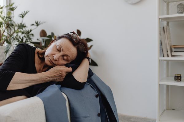 A senior woman in a black top resting on a couch in a minimalist room, conveying calmness and solitude.