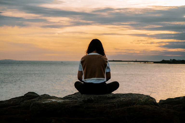 夕阳下坐在海边岩石上的女子背影