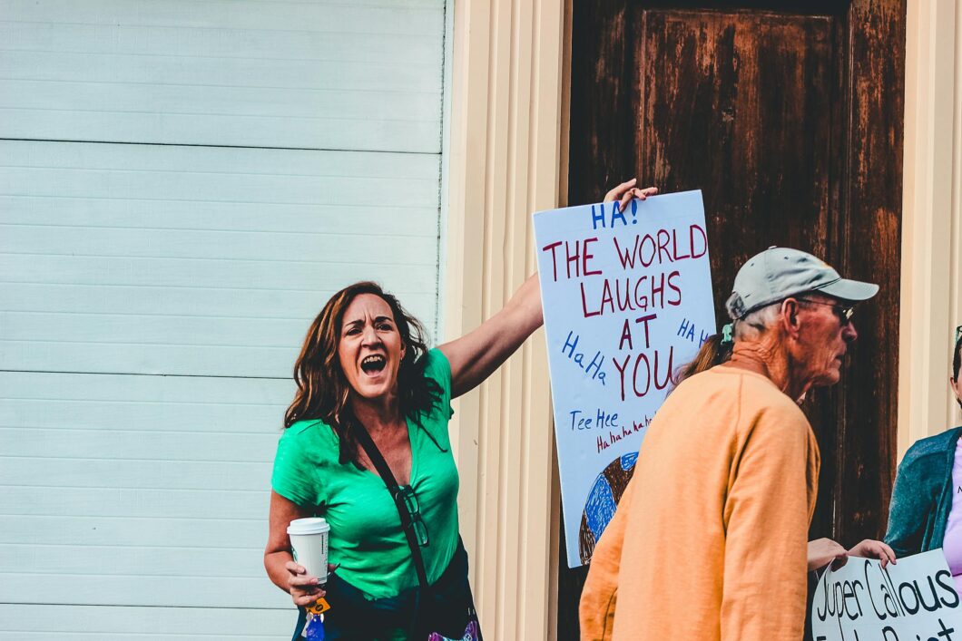 A woman holding a humorous protest sign at an outdoor rally in Wheeling, WV.