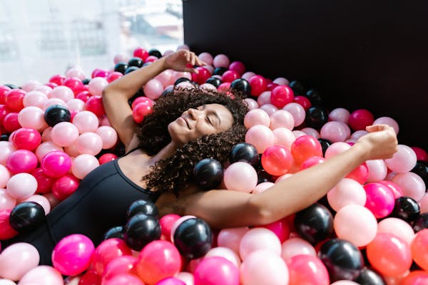 Smiling woman relaxing with closed eyes in a colorful ball pit indoors.