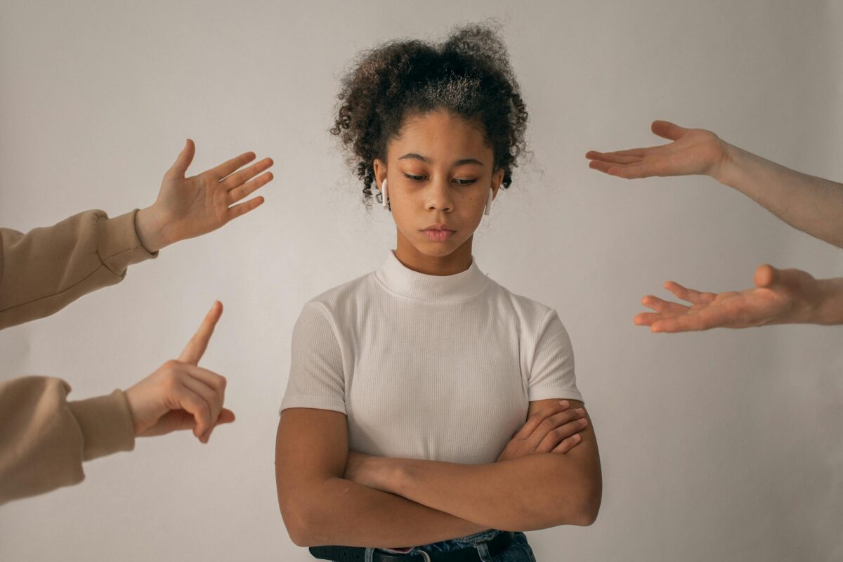 A teenage girl looks upset while expressive hands point and gesture around her.