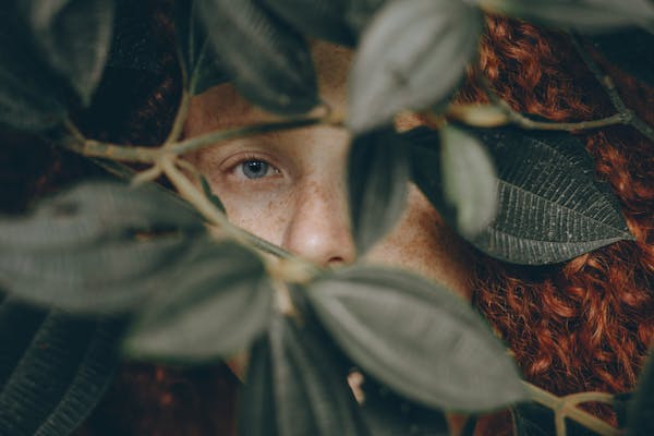 Close-up of a redhead woman partially obscured by leaves, creating an intriguing and mysterious feel.