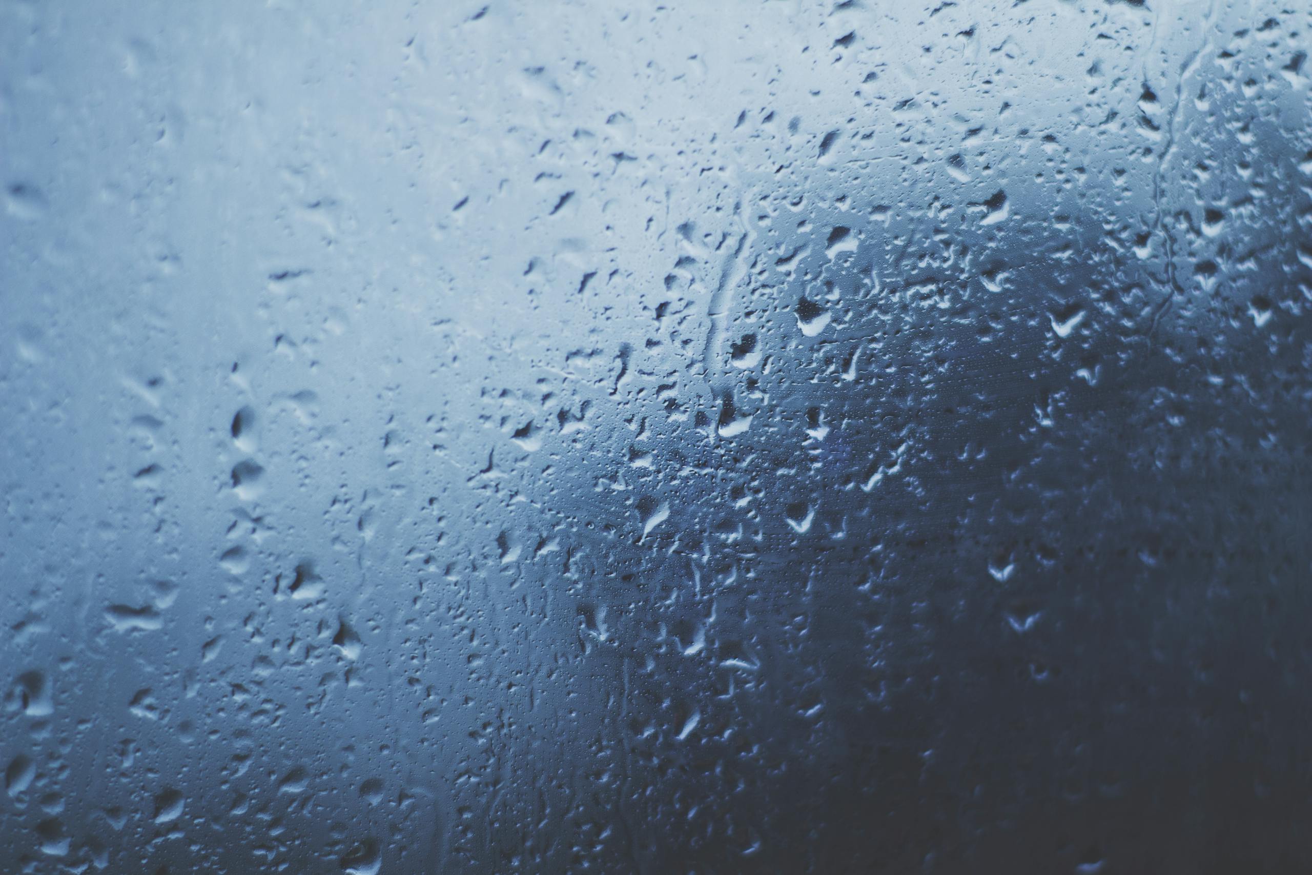 Detailed view of water droplets on a glass window with a blue background.