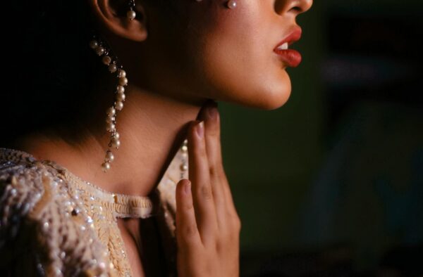 Profile portrait of a woman adorned with pearls and elegant jewelry, set against a dark backdrop.