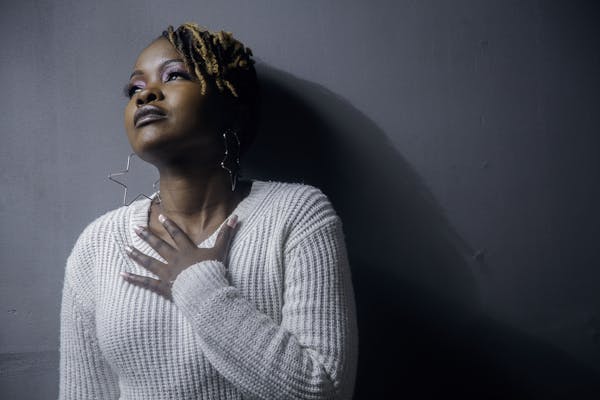 Portrait of a black woman with dreadlocks in a white sweater, looking up thoughtfully indoors.
