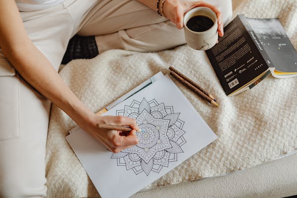 A woman enjoys a cozy moment with coloring, books, and coffee on a soft bed.