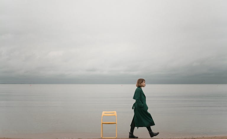 A solitary woman walks by the ocean, capturing calm and introspective solitude.