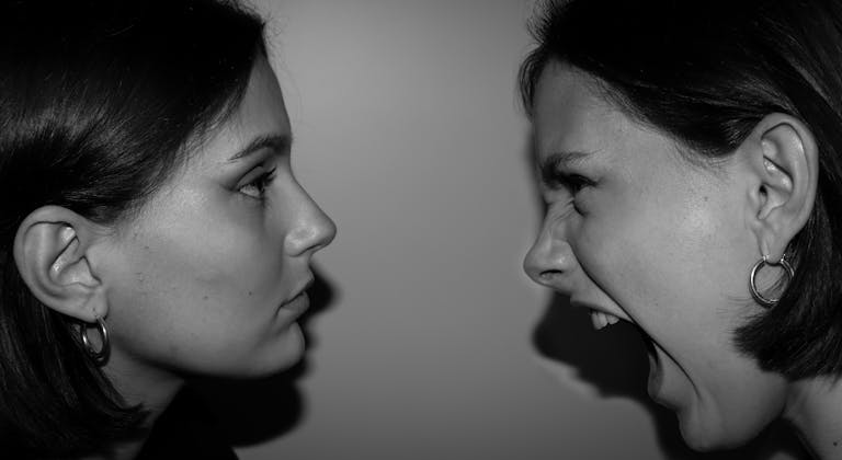 Two women face each other in high contrast, one shouting, depicting raw emotion.