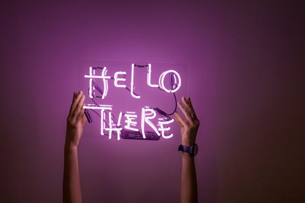 A vibrant neon sign reading "Hello There" held by hands against a purple background.