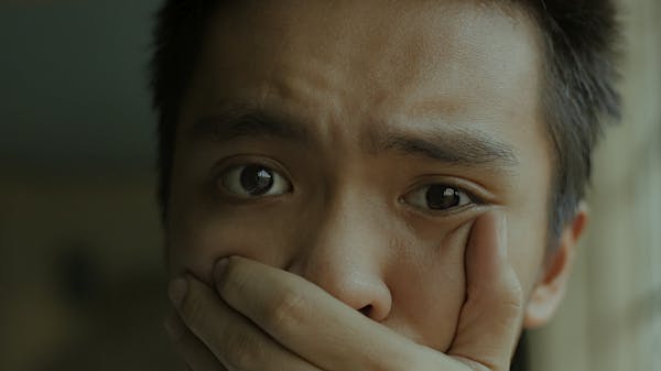 A young man with a distressed expression, covering his mouth.