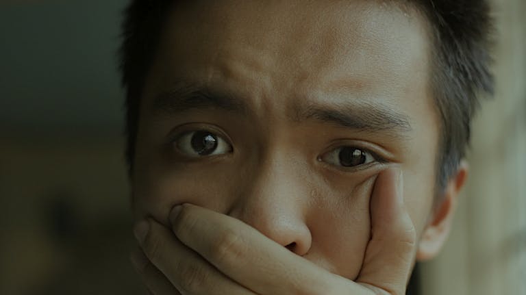 A young man with a distressed expression, covering his mouth.