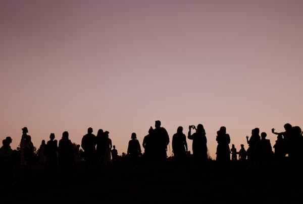Silhouettes of people gathered outdoors during a stunning sunset, creating a captivating scene.