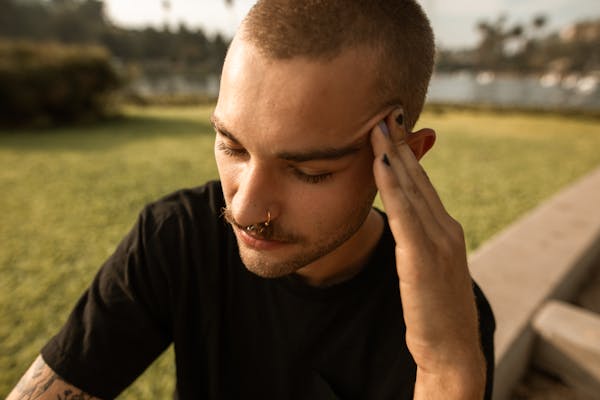 A young man feeling stressed and anxious while sitting outdoors in a park setting.