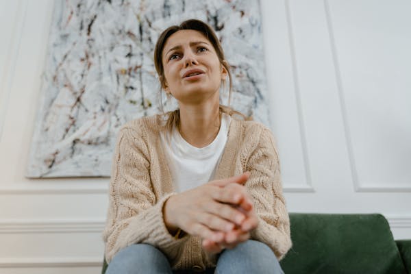 A woman in a cozy sweater is sitting indoors, expressing distress and frustration.