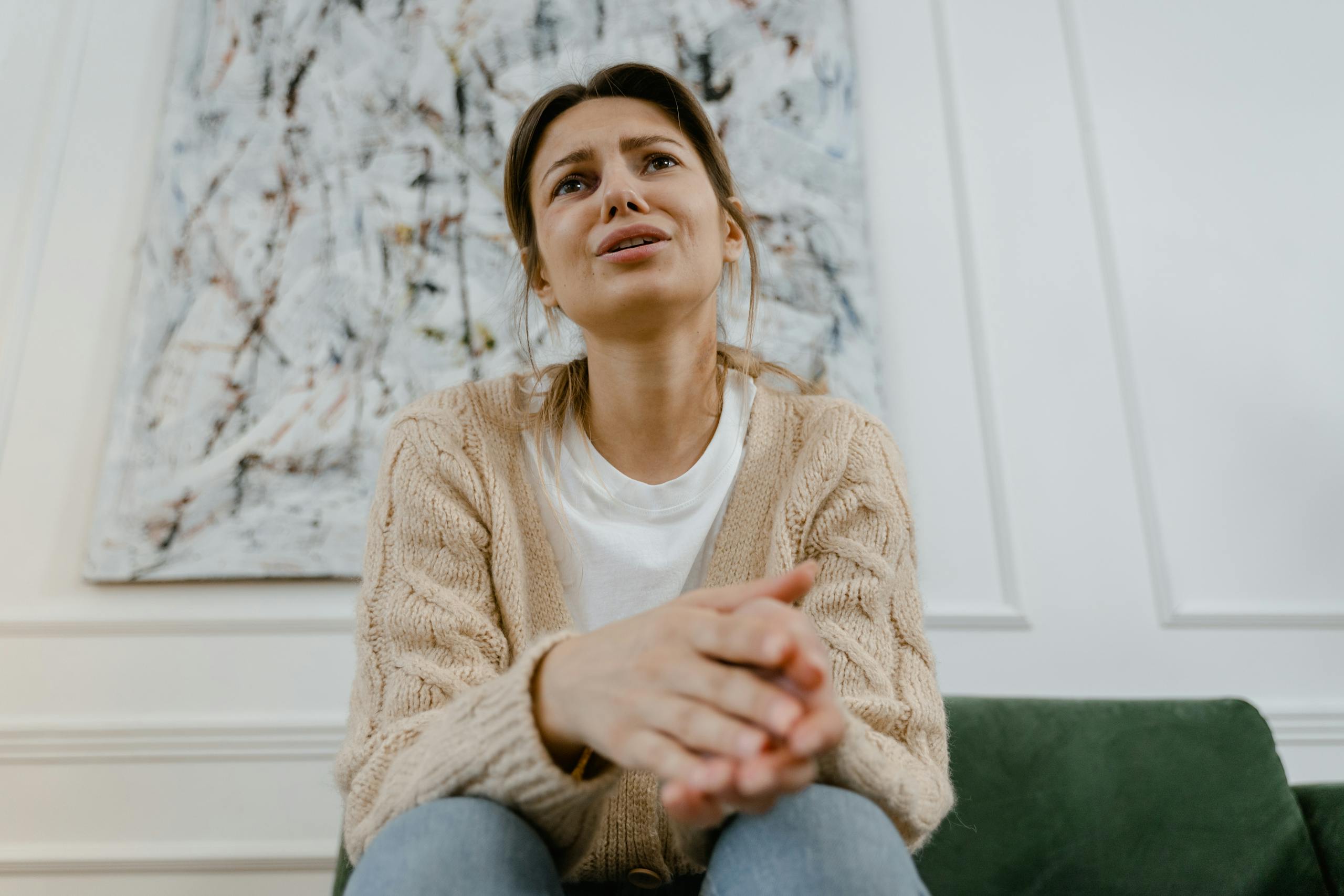 A woman in a cozy sweater is sitting indoors, expressing distress and frustration.
