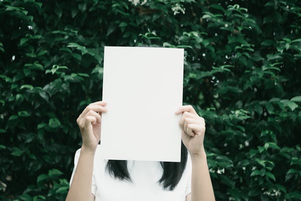 A person holding a blank piece of paper in front of a lush leafy background.