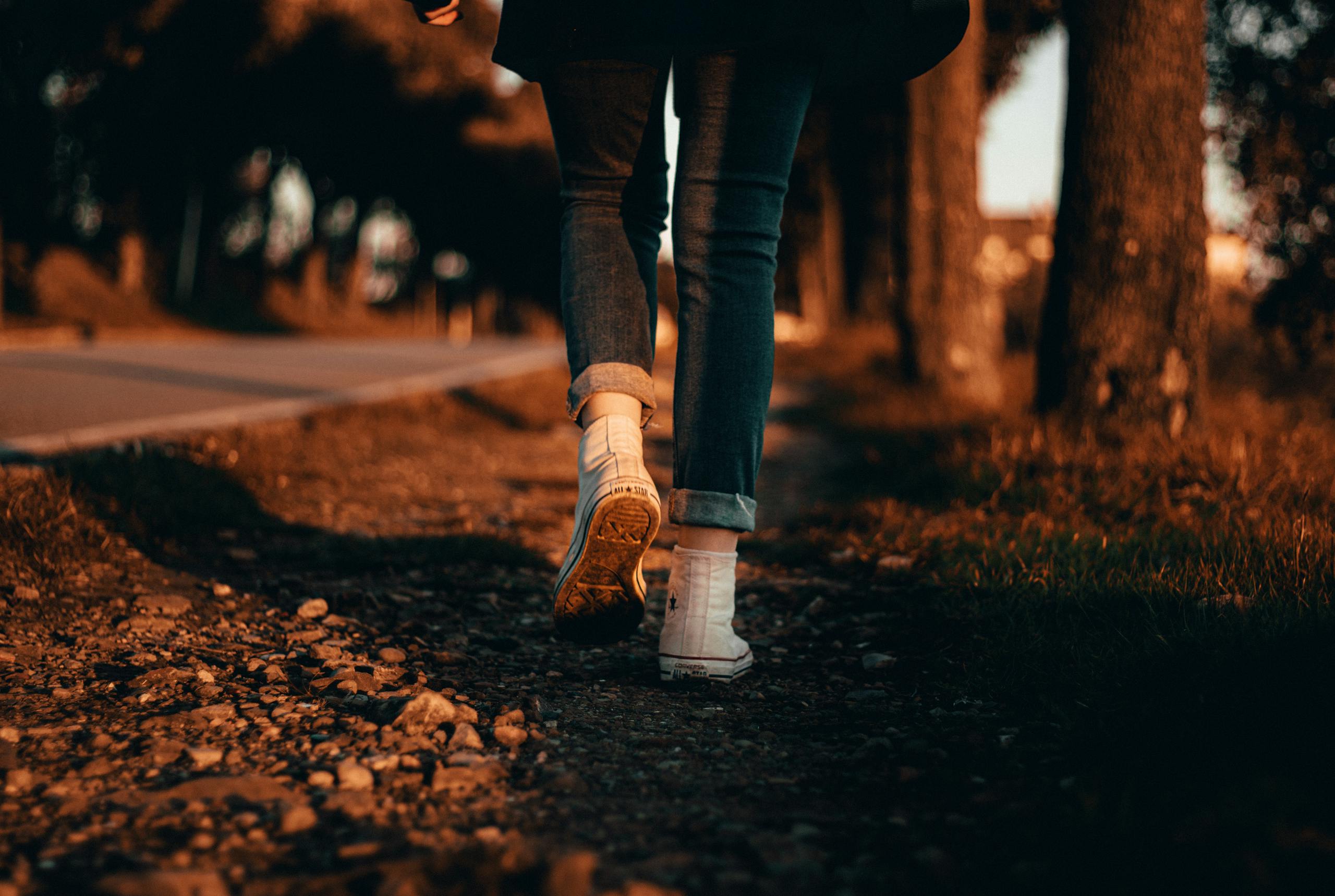A person in jeans and sneakers walks along a forest path at sunset in Italy.