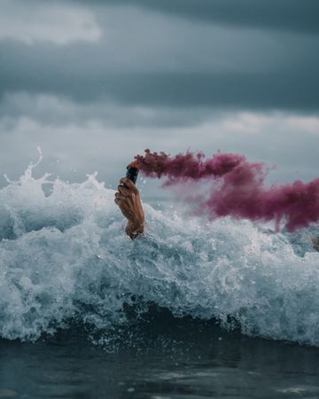 Hand holding a pink smoke bomb amidst crashing waves in Port Elizabeth, South Africa.