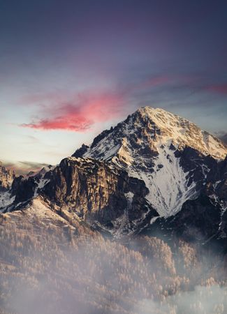 Stunning view of a snow-capped mountain with vibrant sunset hues and low clouds.