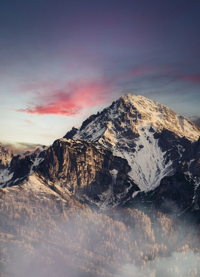 Stunning view of a snow-capped mountain with vibrant sunset hues and low clouds.