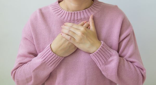 Unrecognizable female wearing pink sweater standing on white background with crossed hands on chest in light room in daytime inside