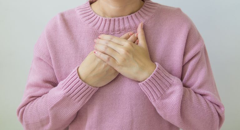 Unrecognizable female wearing pink sweater standing on white background with crossed hands on chest in light room in daytime inside
