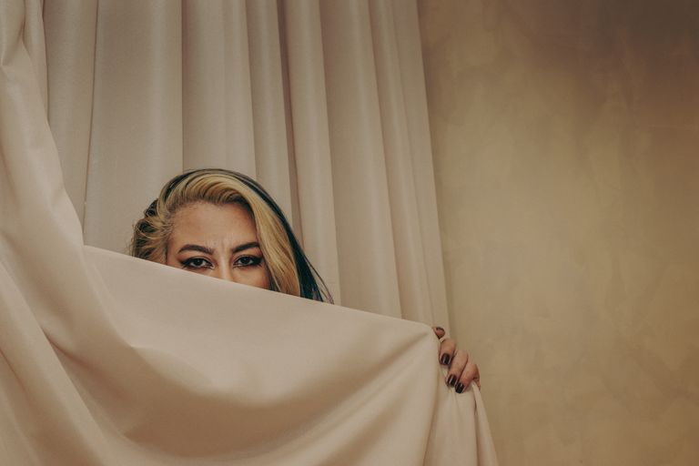 A captivating portrait with a focus on eyes behind a neutral curtain, evoking mystery.