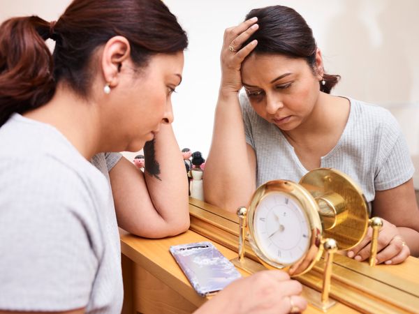 A woman looks pensive and tired, reflecting on burnout with a clock and mirror.