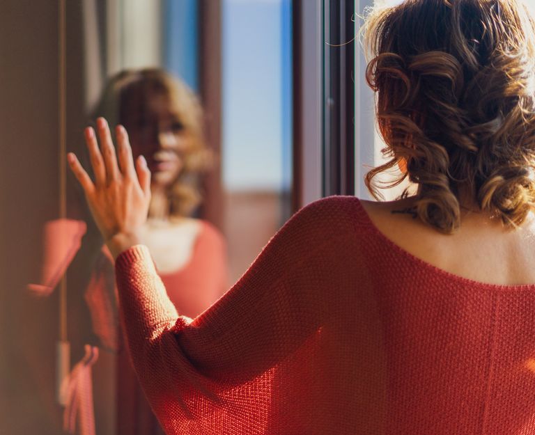 Back view of a woman in red clothing, gazing at her reflection in Madrid.
